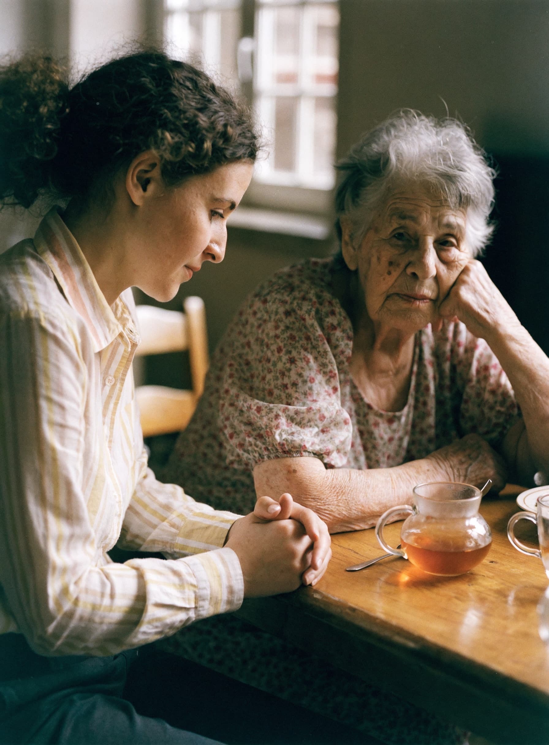 A home carer sharing tea and conversation with an elderly Greek woman at her kitchen table