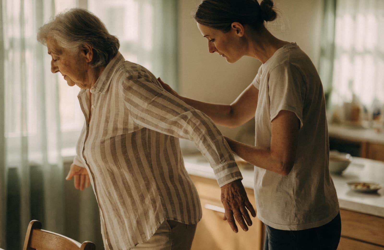 A physiotherapist gently supporting an older woman through a balance exercise in her kitchen